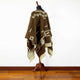 Clint Eastwood alpaca wool poncho – a brown poncho with white geometric patterns drapes over a mannequin, standing on a wooden floor against a plain white wall