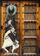 A leather hat and patterned poncho hang on an intricately carved wooden door with geometric designs and metal accents.