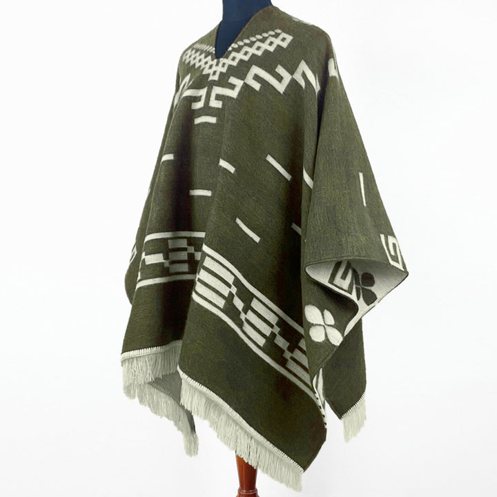 Clint Eastwood alpaca wool poncho – a green poncho with white geometric patterns and fringe edges hangs on a mannequin against a plain white background