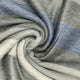 Yatzaputzan baby alpaca wool blanket – a soft, textured fabric drapes in a spiral pattern. The material features alternating gray and blue stripes, creating a soothing, abstract design. The surrounding context is neutral and understated