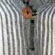 A brown button fastens a gray and white striped woolen fabric, highlighting a fluffy texture and pattern, suggesting a cozy garment setting.