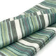 Urauco baby alpaca wool blanket – a folded, striped fabric displays horizontal patterns in shades of green, teal, and white. It rests on a plain white surface, highlighting its soft texture and vibrant colors