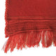 A red woven fabric displays intricate stitching with fringed edges, laid flat against a plain white background, highlighting its texture and vibrant color.