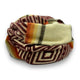 A coiled scarf displays geometric patterns and earthy tones, including maroon, orange, and cream, against a white background.