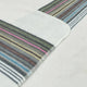 Sigchos baby alpaca wool blanket – a soft blanket lies flat, featuring multi-colored horizontal stripes, including green, pink, and blue, against a white background, with visible stitched edges in an indoor setting