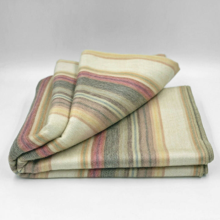 Ducur baby alpaca wool blanket – a folded, multi-striped blanket lies on a white surface, showcasing earthy tones like beige, pink, and gray, creating a cozy and warm appearance