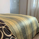 Chalua baby alpaca wool blanket – a striped bedspread covers a bed in a room with sheer curtains and a glass door featuring circular patterns. A patterned pillow is partially visible in the foreground