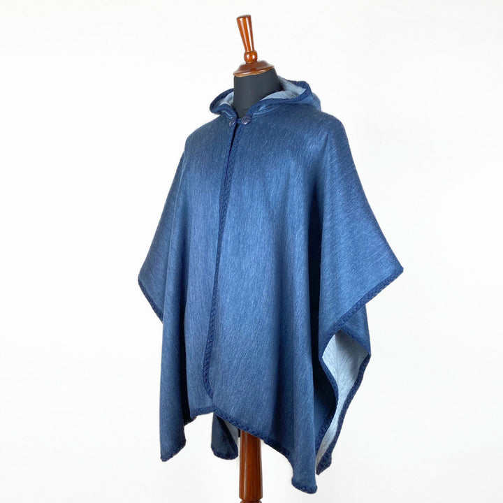 A blue hooded poncho drapes over a mannequin, showcasing its soft, flowing fabric. The poncho is displayed against a plain white background, emphasizing its rich color and texture.