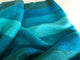 Cajabamba alpaca wool blanket – a soft, striped fabric drapes smoothly, featuring shades of blue and turquoise, creating a serene pattern. The background is a plain, light surface