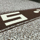 A close-up of a woven mat shows a large, white number 5 on a brown background, surrounded by a white and brown speckled pattern.