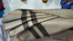 Quisapincha baby alpaca wool blanket – a folded blanket with beige and dark brown stripes rests on a wooden surface. Decorative, colorful hats hang on a white wall in the background