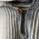 A wooden button secures a black-and-white striped woolen fabric. The close-up highlights the texture and pattern of the material, emphasizing its soft and fuzzy appearance.