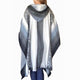 A woman wears a gray and white poncho with a hood, featuring intricate patterns. She stands facing away, showing the back design against a plain white background.