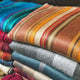 Wholesale lot of 10 queen alpaca wool blankets – stacked colorful wool blankets display horizontal stripes and vibrant patterns. They're layered together on a flat surface, showcasing rich textures and warm hues in a cozy setting