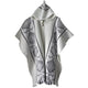 A white poncho with geometric black patterns, featuring a hood and button closure, is displayed against a plain background.