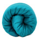Moyaschucho baby alpaca wool blanket – a large, soft teal blanket is tightly rolled into a cylindrical shape, set against a plain, light background
