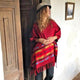A person wearing a red poncho and hat stands leaned against a wooden door, in a rustic setting with white walls and a framed picture.