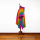 A multicolored striped poncho, displayed on a mannequin, stands in a room with a wooden floor and plain white walls.