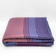 Ochoa baby alpaca wool blanket – a folded blanket rests on a plain surface, featuring a striped pattern in shades of purple and mauve, creating a cozy, textured appearance