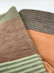 Latacunga alpaca wool throw blanket – a soft, striped blanket features earthy tones of green, brown, and peach. The texture appears fuzzy and thick, suggesting warmth and comfort, laid out on a plain white background