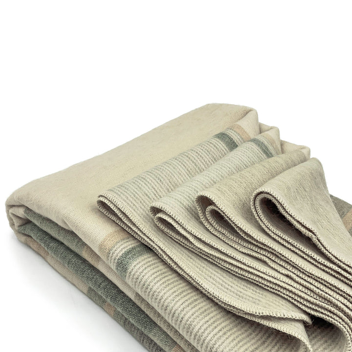 Deleg baby alpaca wool blanket – folded blankets, featuring beige and subtle green striped patterns, are neatly stacked against a plain white background