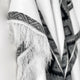 Cuyuja lightweight alpaca wool hooded poncho – a fringed textile drapes elegantly, showcasing intricate dark geometric patterns along the edges, set against a plain background
