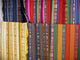 Colorful woven textiles are displayed hanging vertically. Each fabric features intricate geometric patterns with various stripes, and the bold colors range from earthy tones to vibrant reds and greens.