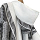Cuyuja lightweight alpaca wool hooded poncho – a white and black patterned fabric poncho drapes on a hanger, displaying a hood and soft texture, set against a plain background