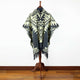 Tarqui alpaca wool hooded poncho – a patterned poncho is displayed on a wooden stand, featuring black and cream geometric designs. The setup is positioned against a plain white wall with a wooden floor
