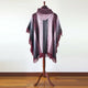 A maroon shawl with fringe hangs on a wooden mannequin stand, positioned in a room with a wooden floor and neutral wall background.