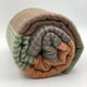 Latacunga alpaca wool throw blanket – a rolled, multi-colored woolen blanket featuring earthy tones of brown, beige, and green with striped patterns sits on a plain white surface