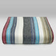 Carihuairazo baby alpaca wool blanket – a folded blanket with wide horizontal stripes in grey, blue, beige, pink, and white hues lies on a plain surface against a neutral gradient background, suggesting a soft texture