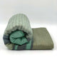 Saquisili baby alpaca wool blanket – a rolled, woolen blanket with green and gray stripes, displayed against a plain, white background. The soft fabric's texture is clearly visible, adding a cozy feel
