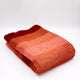 Cusubamba baby alpaca wool blanket – a folded, vibrant orange-red gradient blanket lies on a white surface, creating a cozy and colorful appearance