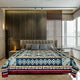 A bed with a geometric-patterned blanket is centered in a modern bedroom. Gray pillows rest against a tufted headboard. Large windows and decorative wall panels enhance the contemporary design.