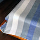 Poguios baby alpaca wool blanket – a striped blanket with blue, grey, and white hues drapes over a wooden surface, set against a dark, wooden floor backdrop