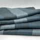 Toacazo baby alpaca wool blanket – a neatly folded, soft, striped blue blanket rests on a flat surface, showcasing its pattern of alternating light and dark shades against a plain background