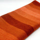 Cusubamba baby alpaca wool blanket – orange fabric with horizontal stripes lies neatly folded, displaying varying shades from vibrant orange to deep red. Set against a plain, white background