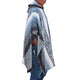 A person is wearing a patterned hooded poncho, standing sideways against a plain white background, while wearing blue jeans.
