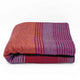 Pallatanga baby alpaca wool blanket – a folded blanket features red, orange, and purple stripes, resting on a plain white background, creating a vivid and cozy appearance
