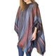 A person wears a striped, multi-colored poncho with fringe detailing, standing against a plain white background.