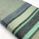 Saquisili baby alpaca wool blanket – a folded woven blanket displays an array of horizontal stripes in varied shades of green and gray. The texture is soft, lying on a plain white surface