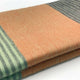 Latacunga alpaca wool throw blanket – a folded blanket displays a checkered pattern with peach and light green stripes, resting on a smooth white surface