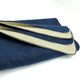 A stack of folded blue denim fabric with visible white edges lies against a plain white background, showing the selvedge detail.