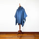 A blue poncho with a hood, draped over a wooden mannequin, stands in a room with a white wall and polished hardwood floor.