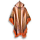 A hooded poncho hangs against a plain background, featuring intricate brown and orange patterns and fringed edges. It is predominantly earth-toned with a central vertical design.