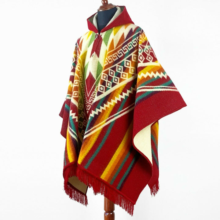 Guismi alpaca wool hooded poncho – a colorful poncho with geometric patterns in red, yellow, and green drapes over a mannequin. The setting is a plain white background, highlighting the poncho's design