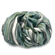 Urauco baby alpaca wool blanket – a crumpled, multicolored striped fabric lies in a heap on a plain white surface, featuring shades of green, gray, and white, creating a soft and textured appearance