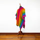 A mannequin displays a vibrant, striped poncho with rainbow colors. It stands in a room with a wooden floor and white walls, creating a colorful focal point against the neutral background.