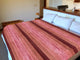 Cusubamba baby alpaca wool blanket – bed with a red-striped blanket is neatly made, positioned in a modern bedroom. Pillows rest against a wooden headboard, with lamps and decorative items on a shelf